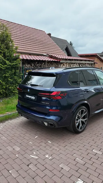 Ciemnoniebieski SUV marki BMW, pokryty folią PPF, zaparkowany na utwardzonym podjeździe przed domem.