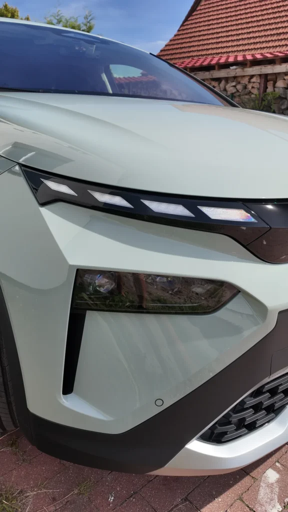 Zbliżenie na przedni róg jasnozielonego SUV-a, na którym widać kanciaste reflektory, czarne wykończenia oraz gładkie, satynowe wykończenie uzyskane dzięki wysokiej jakości folii satynowej.