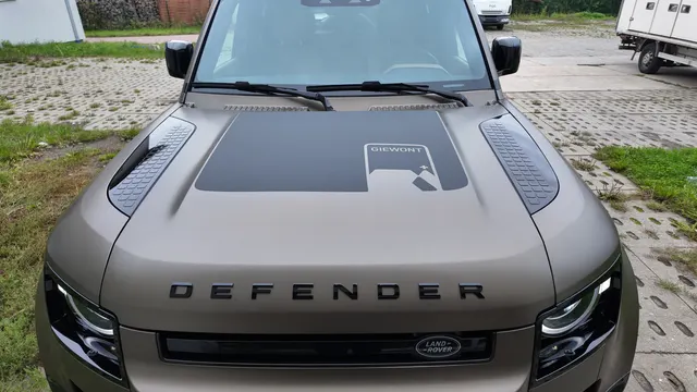 Mata w kolorze brązu na masce samochodu Land Rover Defender z czarną naklejką z napisem GIEWONT.